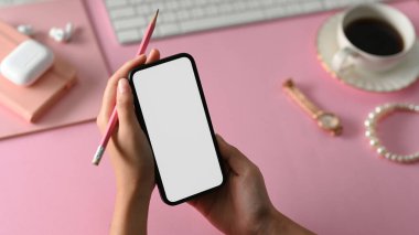 Pembe ofis masasının üzerinde akıllı telefon beyaz ekran maketi ve kalem tutan yaratıcı kadın eli..