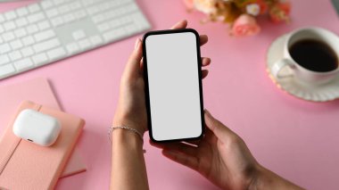 Yakın plan, telefon tutan kadın beyaz ekran modeli kadınsı pembe ofis çalışma masasının üstünde..
