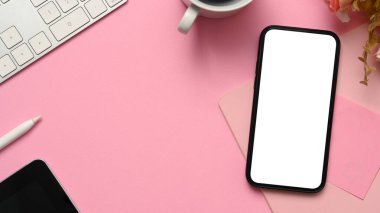 Tepeden çekim, akıllı telefon boş ekran modeli, klavye, kahve fincanı, çiçek ve kopyalama alanı ile pembe çalışma alanı arka planı.