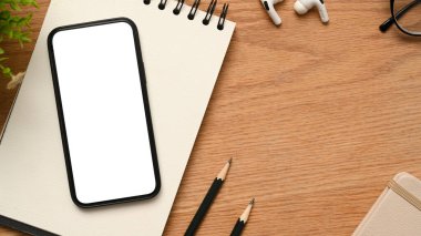 Akıllı telefon boş bir görüntü görüntüsü görüntüsü ekranda, not defterinde, kalemlerde, kulaklıklarda ve ahşap masada. Üst görünüm, düz uzanma