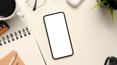 Akıllı telefonu boş ekran maketi, kahve fincanı, not defteri ve aksesuarları olan en az beyaz ofis masası. en üstteki görünüm