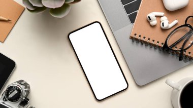 Beyaz ekranlı, kulaklıklı, gözlüklü, dizüstü bilgisayarlı, kameralı ve beyaz masadaki modern rahat çalışma alanının üst görüntüsü.