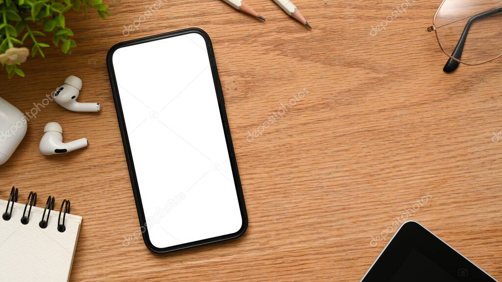 Comfortable workspace with earbuds, glasses, objects and smartphone blank screen mockup on wooden table background. top view