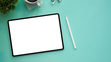 Dijital tablet beyaz ekran maketi, stil kalem, malzeme ve pastel yeşil arkaplan üzerindeki kopyalama alanı ile modern bir çalışma alanının genel görüntüsü.