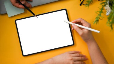 Üst görünüm, odaklanan eller, iki grafik tasarımcısı tasarımlarını yaratıcı sarı ofis masasındaki dijital tablet dokunmatik ped üzerinde tartışıyor. Tablet beyaz ekran modeli.