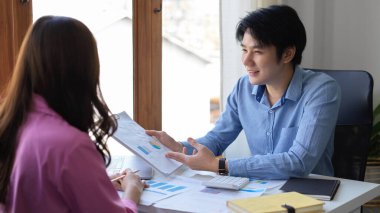 Zeki ve yakışıklı Asyalı genç komisyoncu ofisindeki kadın müşteriye finansal yatırım planını açıklıyor..