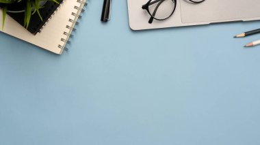 Laptop bilgisayarı, spiral not defteri, aksesuarlar ve kopyalama alanı olan modern mavi ofis masası arka planı.