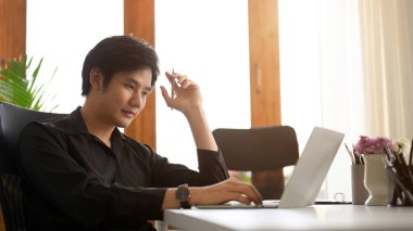 Odaklanmış Asyalı genç işadamı, ofisteki dizüstü bilgisayarına odaklanmıştı.
