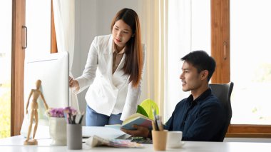 Güzel Asyalı kadın çalışan iş modeli detaylarını ofisteki iş arkadaşına bilgisayar ekranında sunuyor ya da gösteriyor..