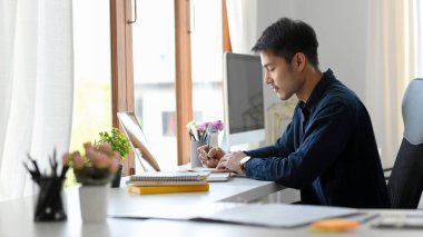 Yakışıklı Asyalı genç işadamı veya erkek patron modern ofis masasında yalnız çalışıyor. yan görünüm