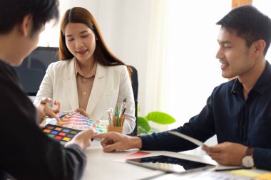 Bir grup grafik tasarımcı beyin fırtınası yapıyor ve ofiste buluşuyorlar, renk örneklerine bakıyorlar.