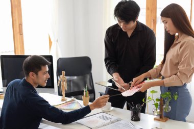 İki grafik tasarımcı stajyeri, patronlarının ofislerindeki projelerine geri bildirim yapmalarını dinlerler..