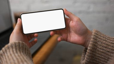 Bulanık bir arkaplan üzerinde yatay pozisyonda cep telefonu beyaz ekran modeli tutan kadın eller..