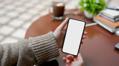 Açık hava parkındaki kafede cep telefonunu sehpanın üzerinde tutan kadın eller. Akıllı telefon boş ekran.