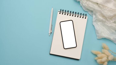 Spiral not defterinde cep telefonu boş ekran modeliyle minimal pastel mavi ofis masası arka planı.