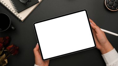Üst Manzara, bir iş kadını elleri tablet dokunmatik ekranı tutuyor modern siyah ofis masasının üzerinde ofis aksesuarlarıyla beyaz ekran maketi..