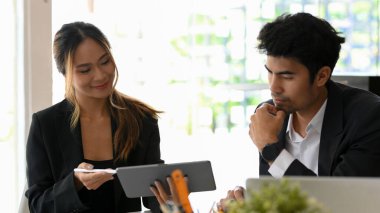 Asyalı bayan asistan, tablet ekrandaki verileri ofisteki profesyonel erkek patronuna gösteriyor.