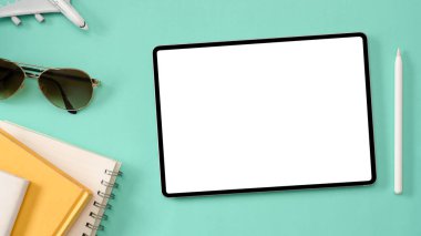 Tepeden çekim, Tablet boş ekran görüntüsü montaj için motifiniz güneş gözlüğü, uçak, not defteri ve stil kalemli yeşil arkaplan grafiğiniz.