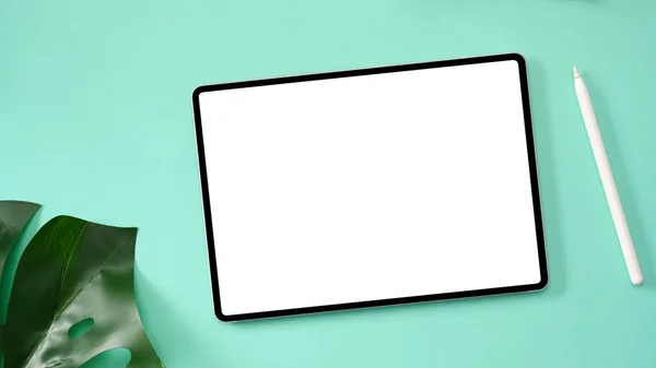 オーバーヘッドショット デジタルタブレットタッチパッドホワイトスクリーンモックアップ 緑の背景にスタイラスペンとモンスターリーフ — ストック写真
