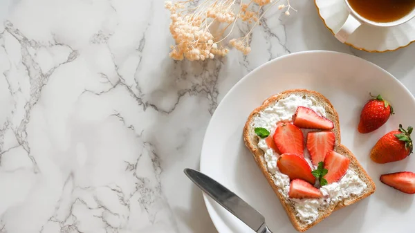 健康的吐司 新鲜草莓和自制的白盘奶酪 配上一杯茶和白色大理石桌子背景 顶部视图 — 图库照片