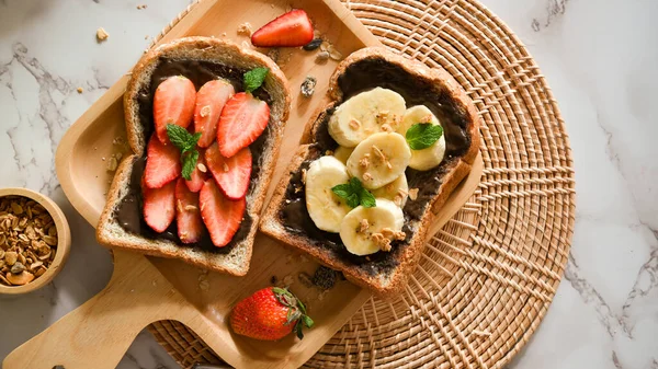 俯瞰全景 健康的烤面包 草莓和香蕉 黑巧克力铺在木盘上的全麦面包上 — 图库照片