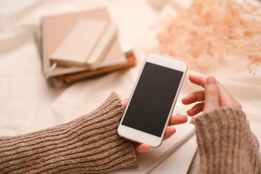 Yakın plan, sıcak süveter giyen kadın blogcu sosyal medyasını kontrol etmek için akıllı telefon kullanıyor. telefon siyah ekran modeli.