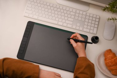 Üst görünüm, kırpılmış resim, kadın grafik tasarımcısı, sanatçı veya mimar grafik tablet kullanarak ve ofis masasındaki bilgisayar ekranına bakarak.