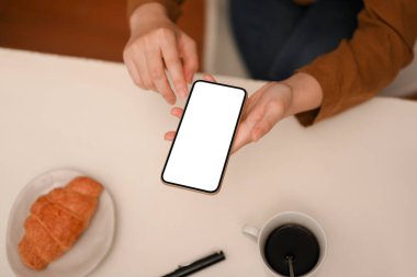 Üst manzara, kadın akıllı telefonuyla e-postalarını kontrol ederken kahvaltını kahve dükkanında yapıyor. akıllı telefon beyaz ekran modeli.