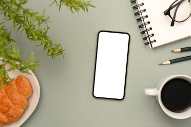 Üst manzara, ofis kağıtlı modern ofis masası, akıllı telefon beyaz ekran modeli, gri arka planda bir fincan kahve ve kruvasan..