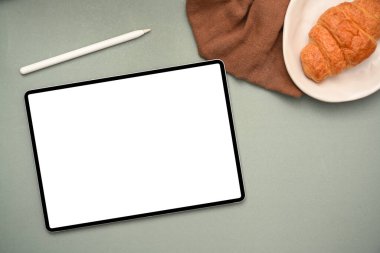 Kablosuz tablet dokunmatik dokunmatik ekran modeli, stil kalem ve kruvasan ile yukarıdaki ofis çalışma alanı yeşil arka planı.