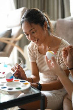 Portre, güzel Asyalı kadın arkadaşlarıyla oturma odasında Paskalya yumurtası boyuyor. Paskalya bayramı partisi.