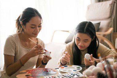 Paskalya tatili konseptinde mutlu aile zamanları, kız kardeşiyle birlikte oturma odasında Paskalya yumurtası boyayan Asyalı çekici bir kadın..