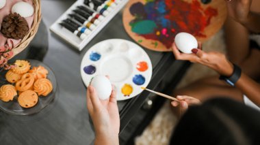 Yakın çekim ve daha yukarıdaki görüntüde, anne ve kızı evde suluboya ile bir Paskalya yumurtası boyuyor. Paskalya tatili aktiviteleri.