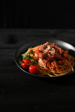 Domates soslu lezzetli spagetti ve siyah tabakta parmesan peyniri..