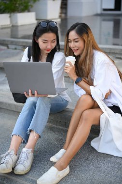 İki çekici Asyalı üniversite öğrencisi merdivenlerde dizüstü bilgisayar kullanıyor ve birlikte web sitesinde ilginç bir şeyler arıyorlar..