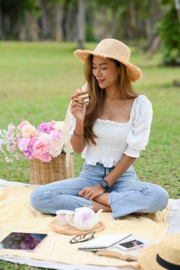 Muhteşem Asyalı kadın dışarıda piknik yapıyor, kek yiyor ve ikindi çayı içiyor. Yaşam tarzları konsepti.