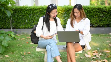 Yeşillik parkında bankta oturan iki çekici Asyalı genç üniversite öğrencisi dizüstü bilgisayar ekranında bazı detaylara bakıyorlar. Üniversitenin hayat konsepti