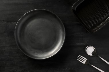 Siyah yemek masasında gümüş takımlı boş seramik tabak. en üstteki resim.