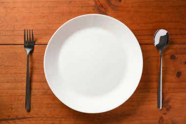 Boş beyaz seramik tabak ve ahşap masada gümüş çatal bıçak ile üst görünümü ayarlayan basit bir yemek masası..