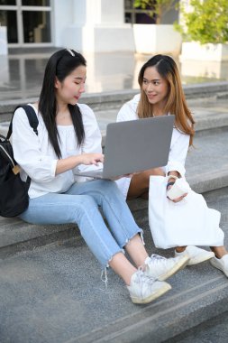 Çekici Asyalı genç kız öğrenci proje sunumunu sınıf arkadaşına gösteriyor, kampüs merdivenlerinde birlikte oturuyor..