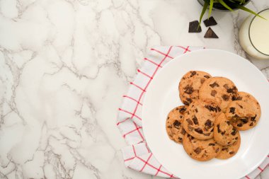 Beyaz mermer zemin üzerine yazdığınız metin için beyaz tabakta bir bardak süt ve fotokopi alanı olan lezzetli çikolatalı yumuşak kurabiyeler. en üstteki görünüm.