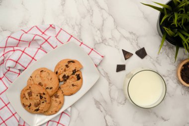 Manzaranın üstünde, kahvaltı konsepti için lezzetli hamur işleri. Beyaz mermer masa üzerinde bir tabak kurabiye ve bir bardak süt..