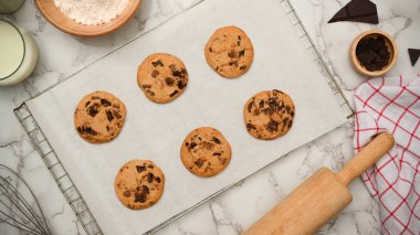 Üst manzara, düz uzanma, taze pişmiş yumuşak kurabiyeler kabartma çarşafında çikolata parçaları, merdane ve bir kase kabartma tozu.