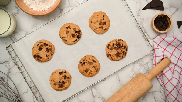 Üst manzara, düz uzanma, taze pişmiş yumuşak kurabiyeler kabartma çarşafında çikolata parçaları, merdane ve bir kase kabartma tozu.
