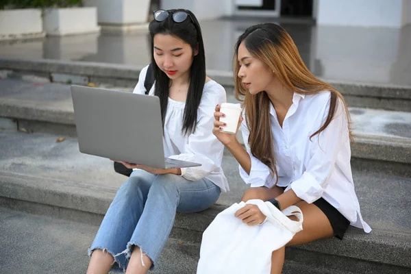Kampüs binasının önünde merdivenlerde oturmuş dizüstü bilgisayar kullanan genç kız öğrenciler..