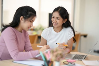 Güzel ve neşeli Asyalı bayan çalışanı, iş arkadaşını, ofisteki mali verileri analiz etmesi için eğitiyor..