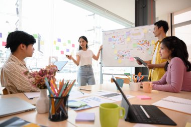 Asyalı iş adamları ofiste atölye ile buluşuyor, beyin fırtınası yapıyor, pazarlama fikirlerini tartışıyor ve süreci toplantı odasında birlikte beyaz tahtada planlıyorlar..