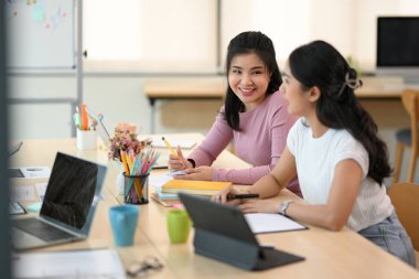 İki neşeli Asyalı kadın işçi birlikte çalışırken ve beyin fırtınası yaparken güzel bir sohbet ediyorlar.