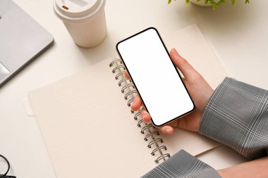 Üst görünüm, bayan eller akıllı telefonu boş tutarken minimum beyaz ofis masası üzerinde boş ekran.