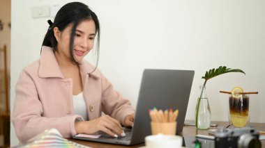 Güzel kadın grafik tasarımcısı çalışıyor, projesini temizliyor ve dizüstü bilgisayarından grafik tasarımını kontrol ediyor..